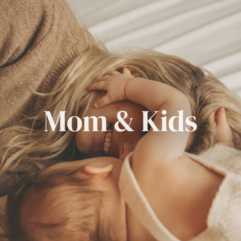 A mother and her young child sharing a tender, joyful moment together with the child smiling and reaching up to her — representing the Mom & Kids category supporting family wellness from infants to growing children