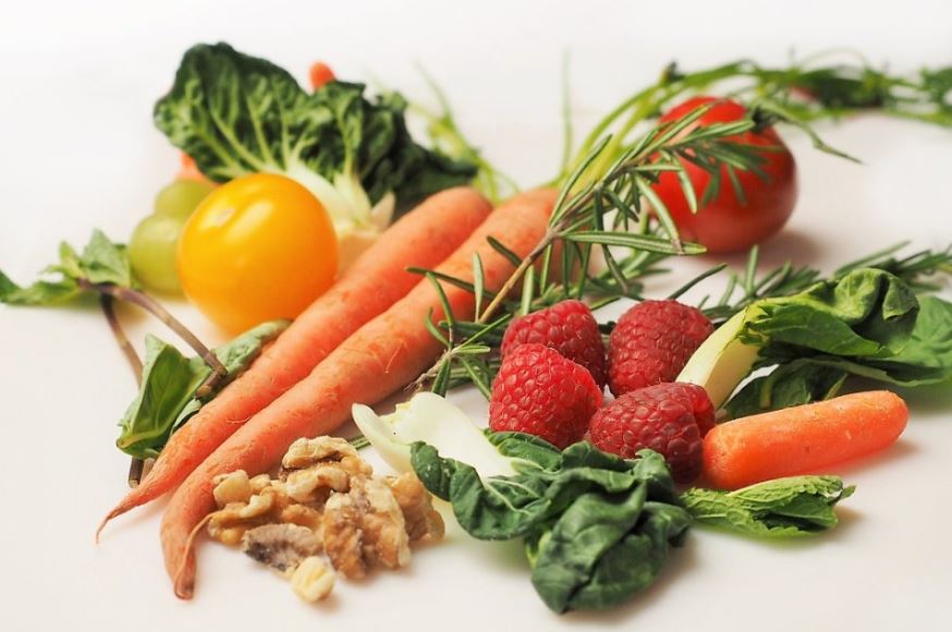 Fresh carrots, tomatoes, raspberries, spinach, walnuts, and rosemary arranged on a white background, representing the plant-based ingredients behind vegan collagen