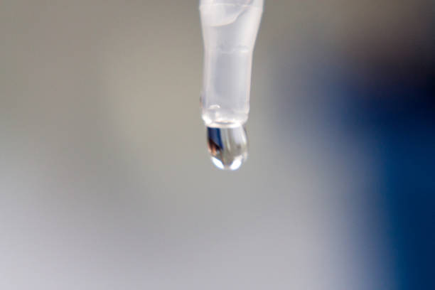 Close-up of a single artificial tear drop about to fall from a preservative-free vial