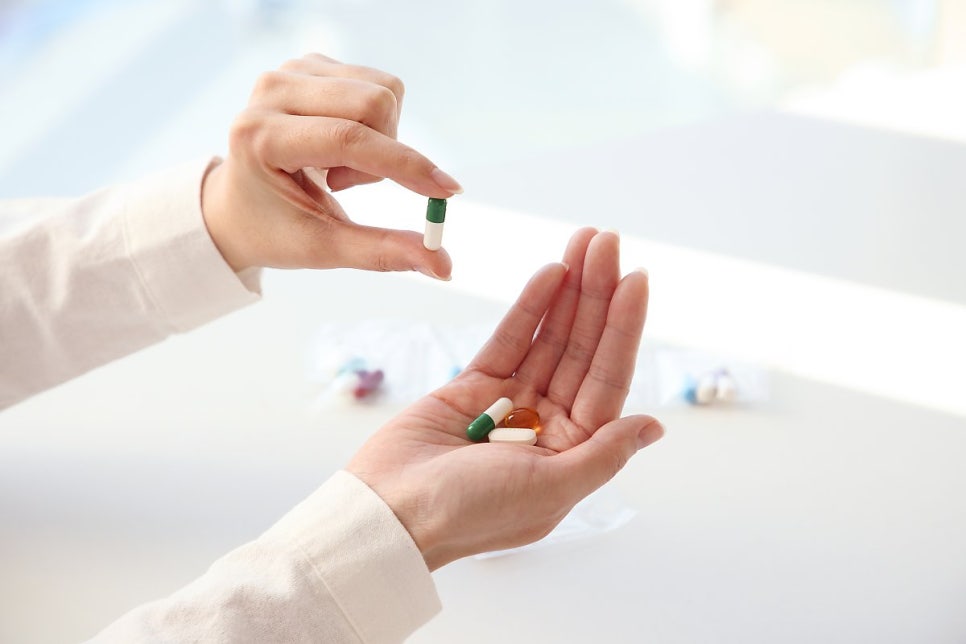 Hand holding a capsule above a palm of mixed supplements