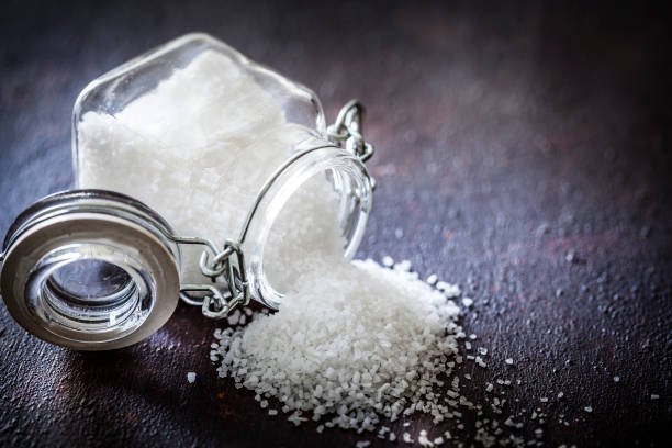 Coarse salt spilling from a glass jar, representing excess dietary sodium
